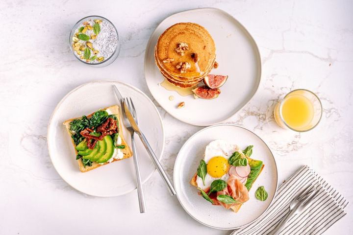 Aerial view of a delicious and healthy breakfast with pancakes, avocado toast, and refreshing drinks.