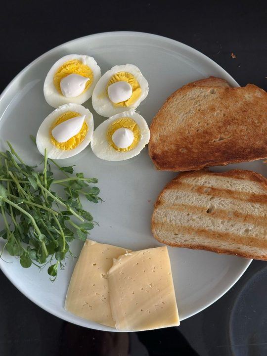 A balanced breakfast featuring hardboiled eggs, cheese slices, toasted bread, and fresh greens.