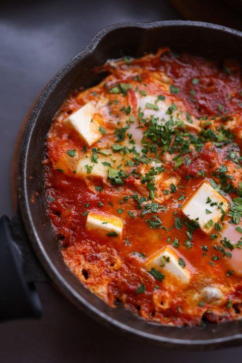 Hot and savory shakshuka with poached eggs and feta cheese in a rustic skillet.