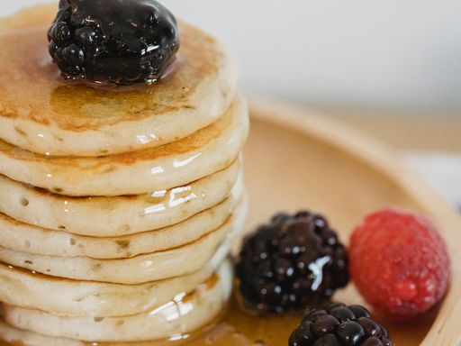 Stack of fluffy pancakes topped with mixed berries and syrup on a wooden plate.