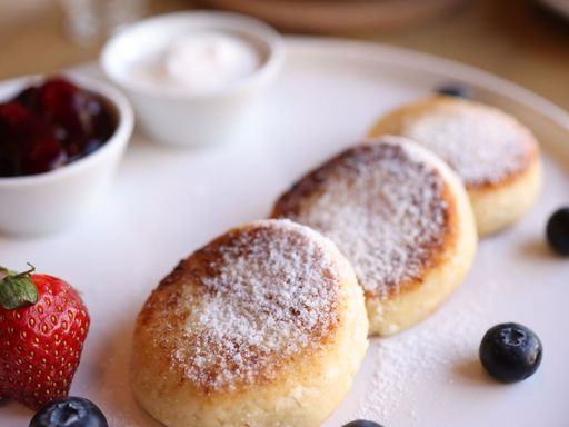 Tasty syrniki served with strawberries, blueberries, and cream, perfect for breakfast.