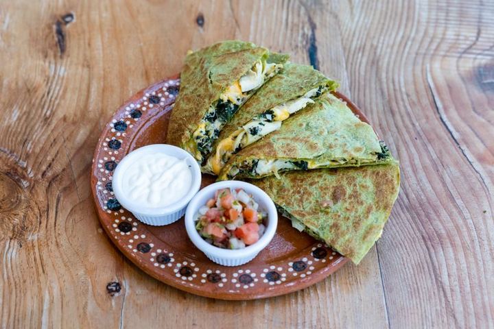 Delicious spinach and cheese quesadilla with sour cream and salsa on a rustic wooden table
