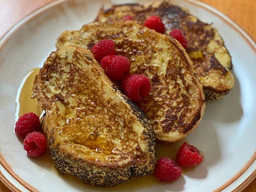 Golden-brown French toast topped with raspberries and syrup.