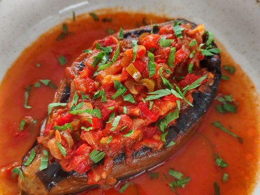 Stuffed eggplant with spices and red sauce on a white plate.