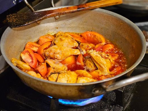 Chicken pieces and tomatoes simmering in a pan on the stove