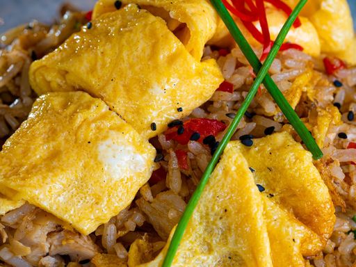 Egg fried rice with red peppers and chives served in a blue bowl.
