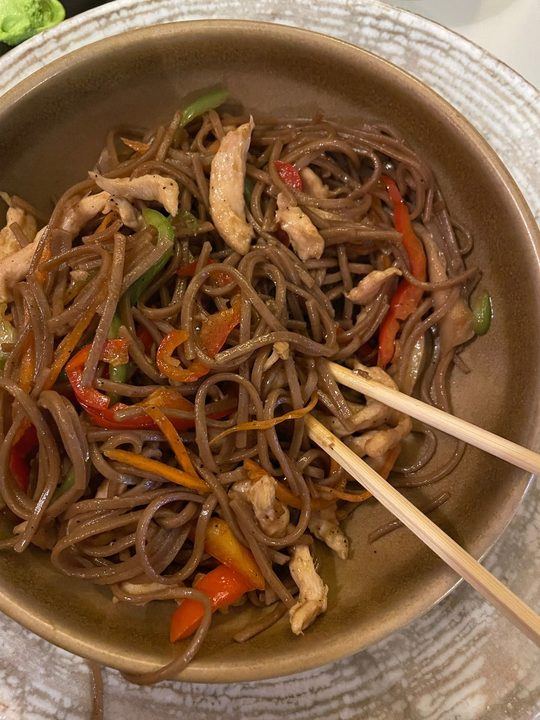 A mouthwatering soba noodle stir-fry with bell peppers and chicken in a ceramic bowl.