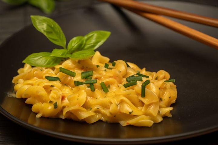 Close-up of creamy pasta on a black plate garnished with basil and chives.