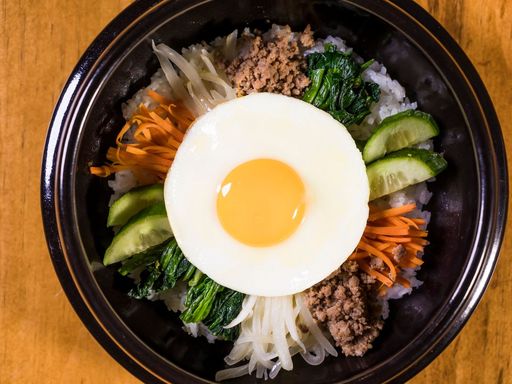 Korean bibimbap with egg, rice, and fresh vegetables in a bowl.
