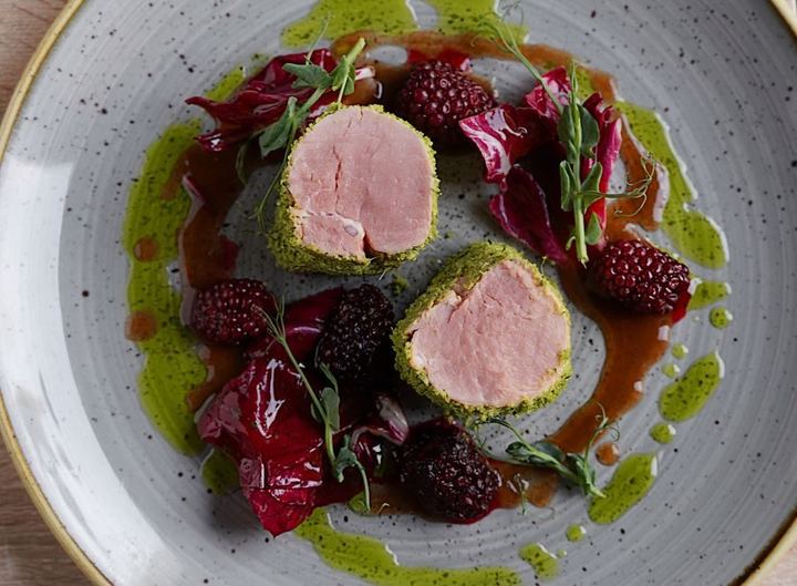 Elegant gourmet pork tenderloin dish garnished with fresh raspberries and vibrant greens.