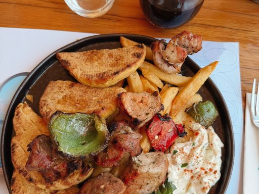 Greek souvlaki served with tzatziki, roasted vegetables, and wedges.