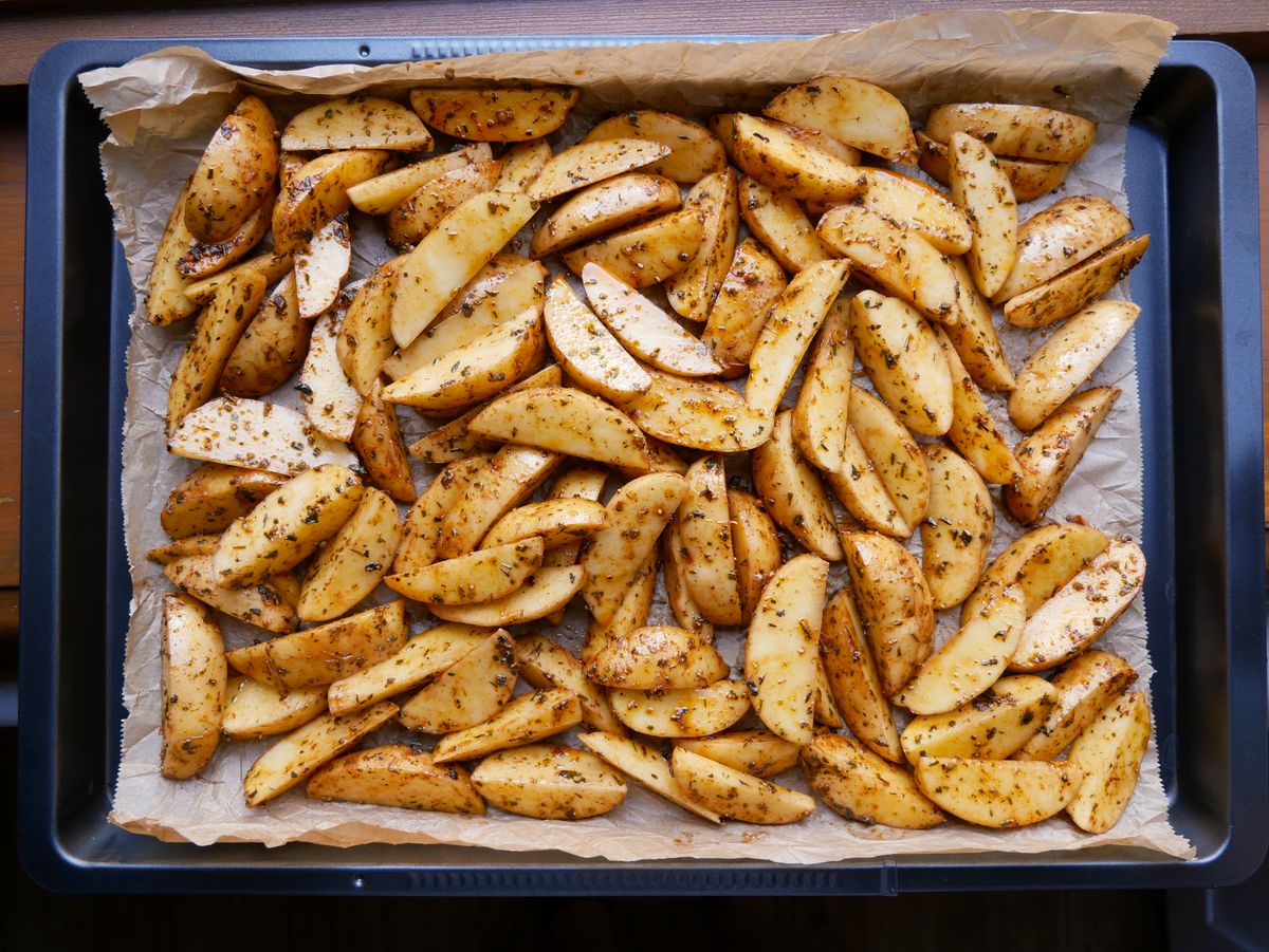 Roasted potato wedges seasoned with herbs on a baking tray.