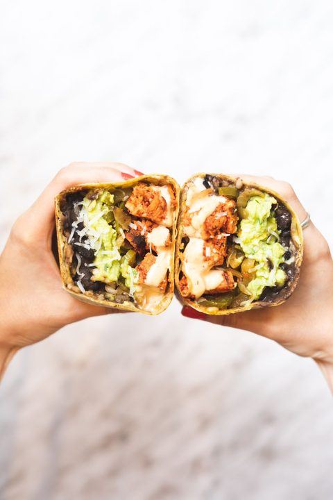 Tasty burrito filled with vibrant ingredients, held by hands, perfect for Mexican cuisine lovers.