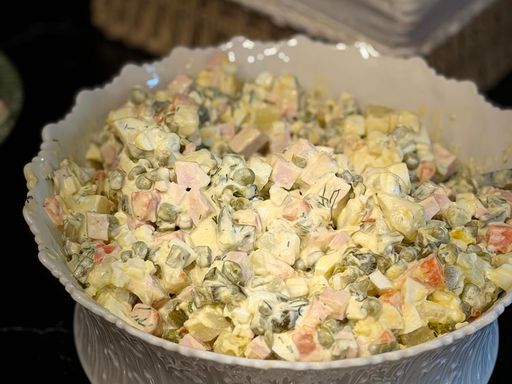 Delicious homemade Russian Olivier salad with peas, carrots, and potatoes in a decorative bowl.