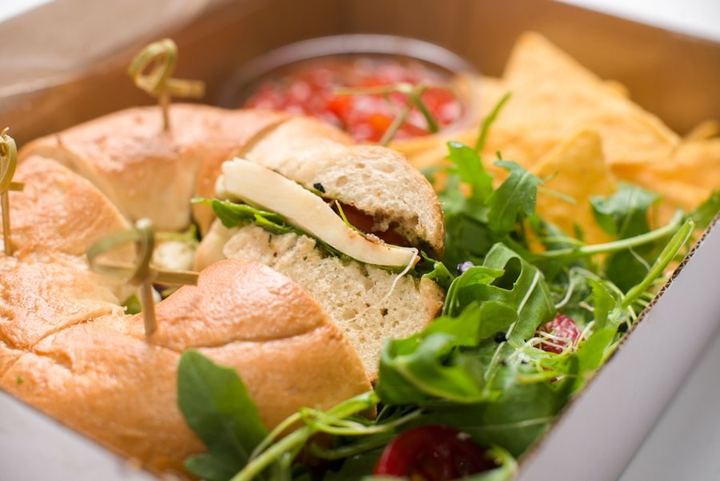 Delicious bagel sandwich with arugula and cheese garnished with salad in a takeout box.