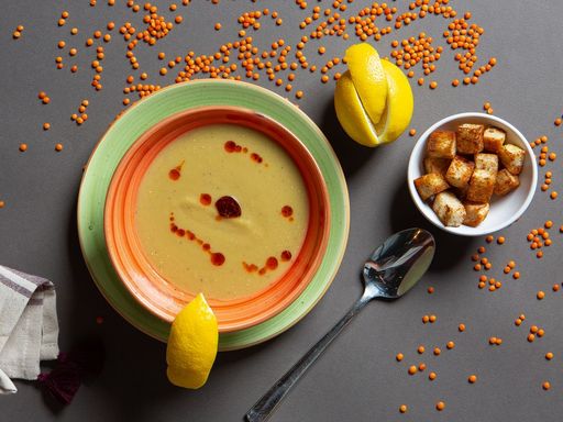 Red lentil soup garnished with lemon wedges and croutons.