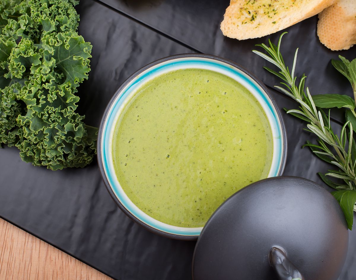 A flavorful green soup garnished with fresh kale and herbs.