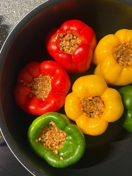 Top view of colorful stuffed bell peppers filled with grains in a black pot.