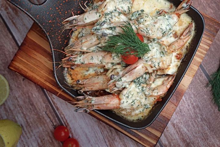 Sautéed shrimp in creamy sauce with dill and cherry tomatoes in an iron skillet.