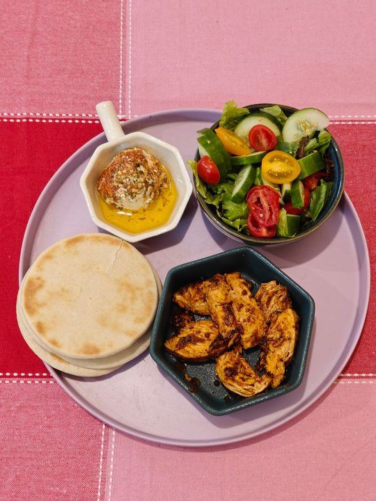 Colorful Mediterranean dish featuring salad, grilled chicken, hummus, and pita bread.
