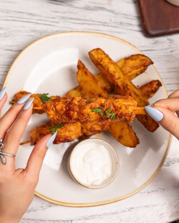 Crispy chicken skewers with seasoned potato wedges and creamy dip on a plate.